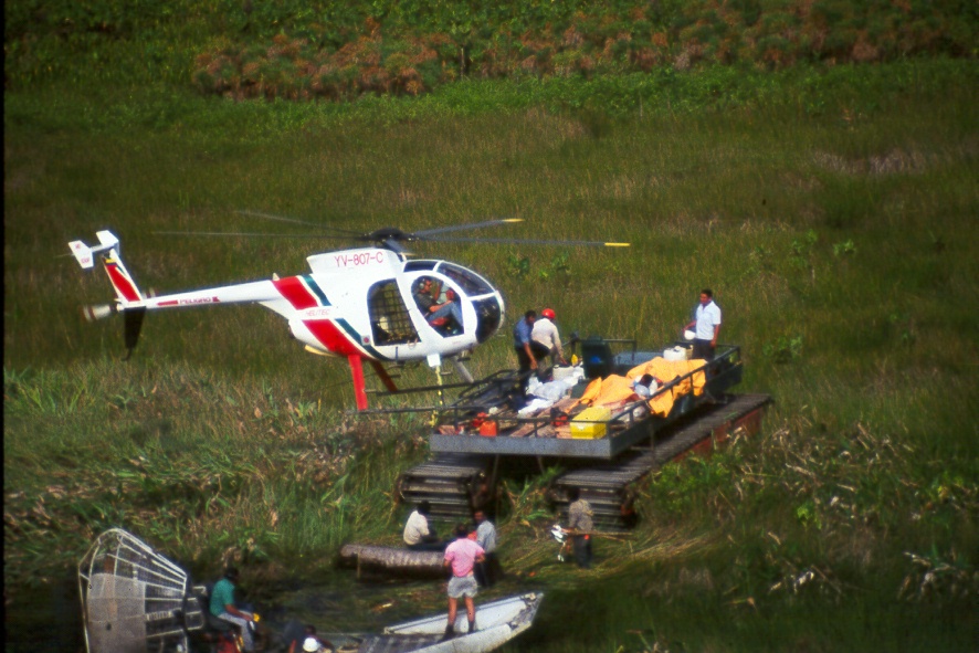 Helicóptero Helitec (YV-807-C) junto a plataforma de carga en zona de pantano, con personal en botes